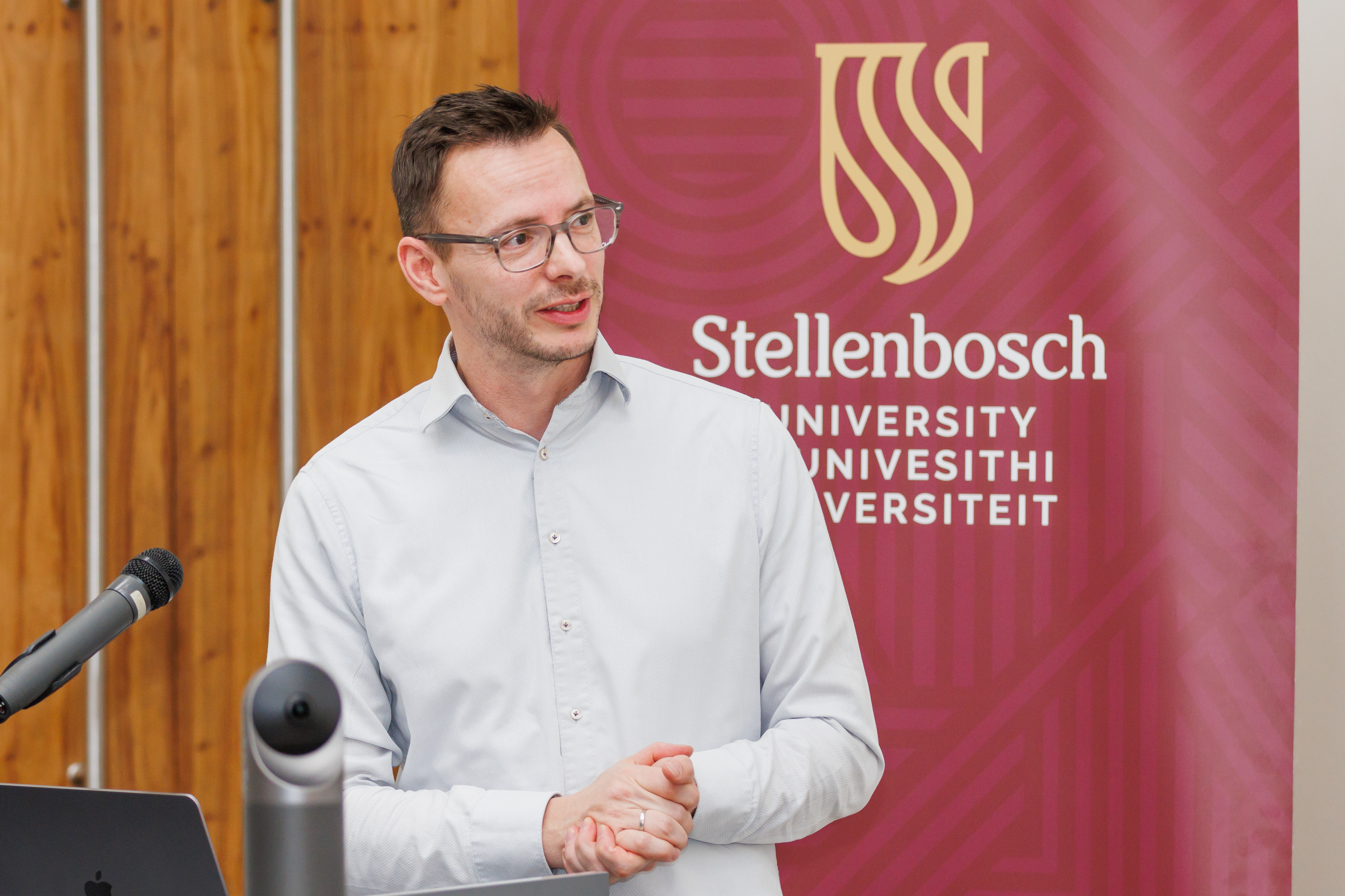 Presenter in front of a stellenbosch university banner in an auditorium delivering a speech