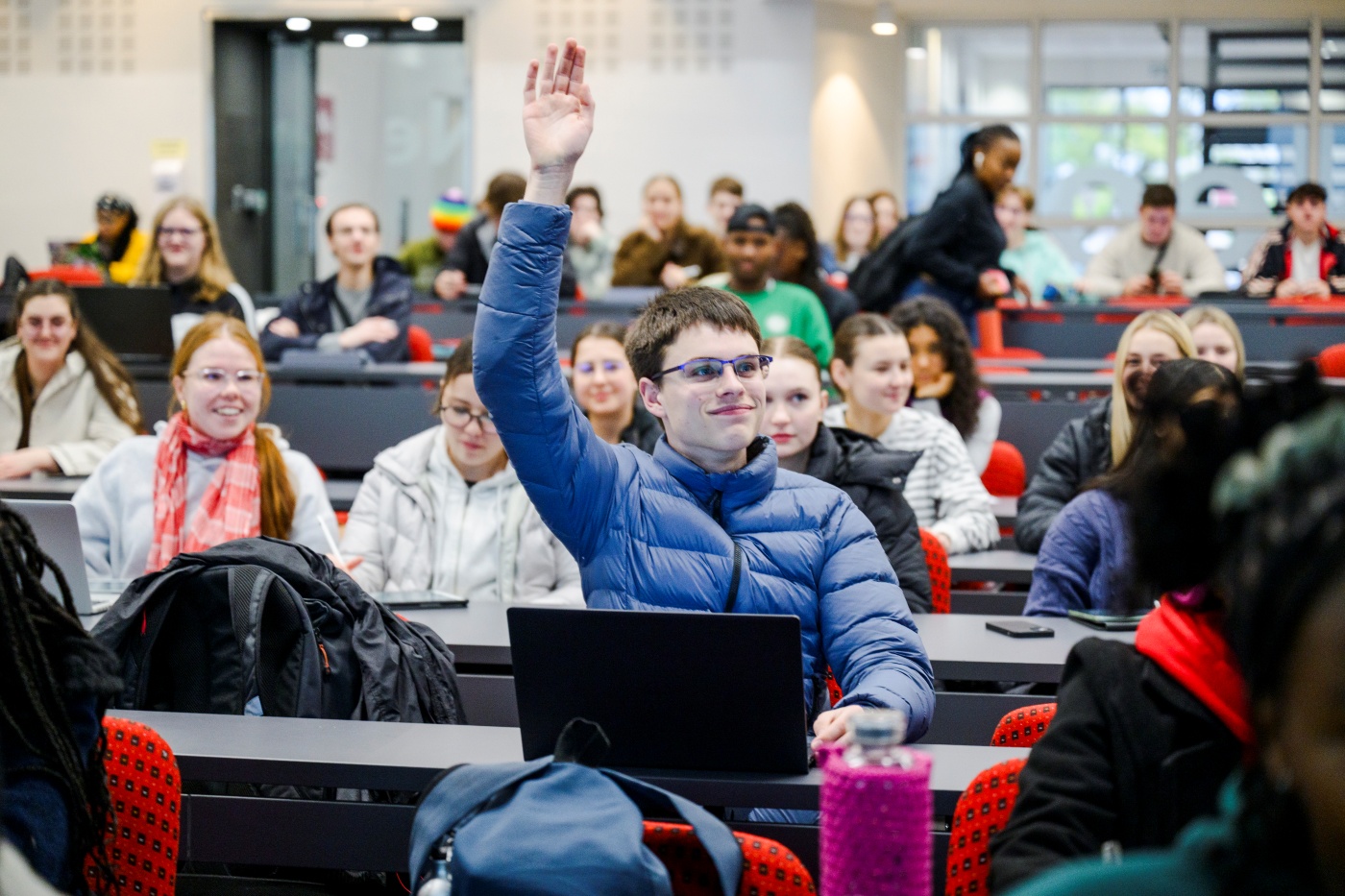 A firrst-year science student raises his hand high to ask a question during a chemistry lecture.