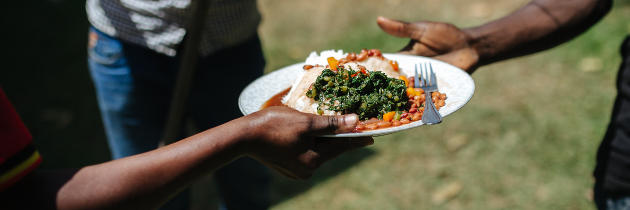 A picture of one person handing a plate of African food to another person.