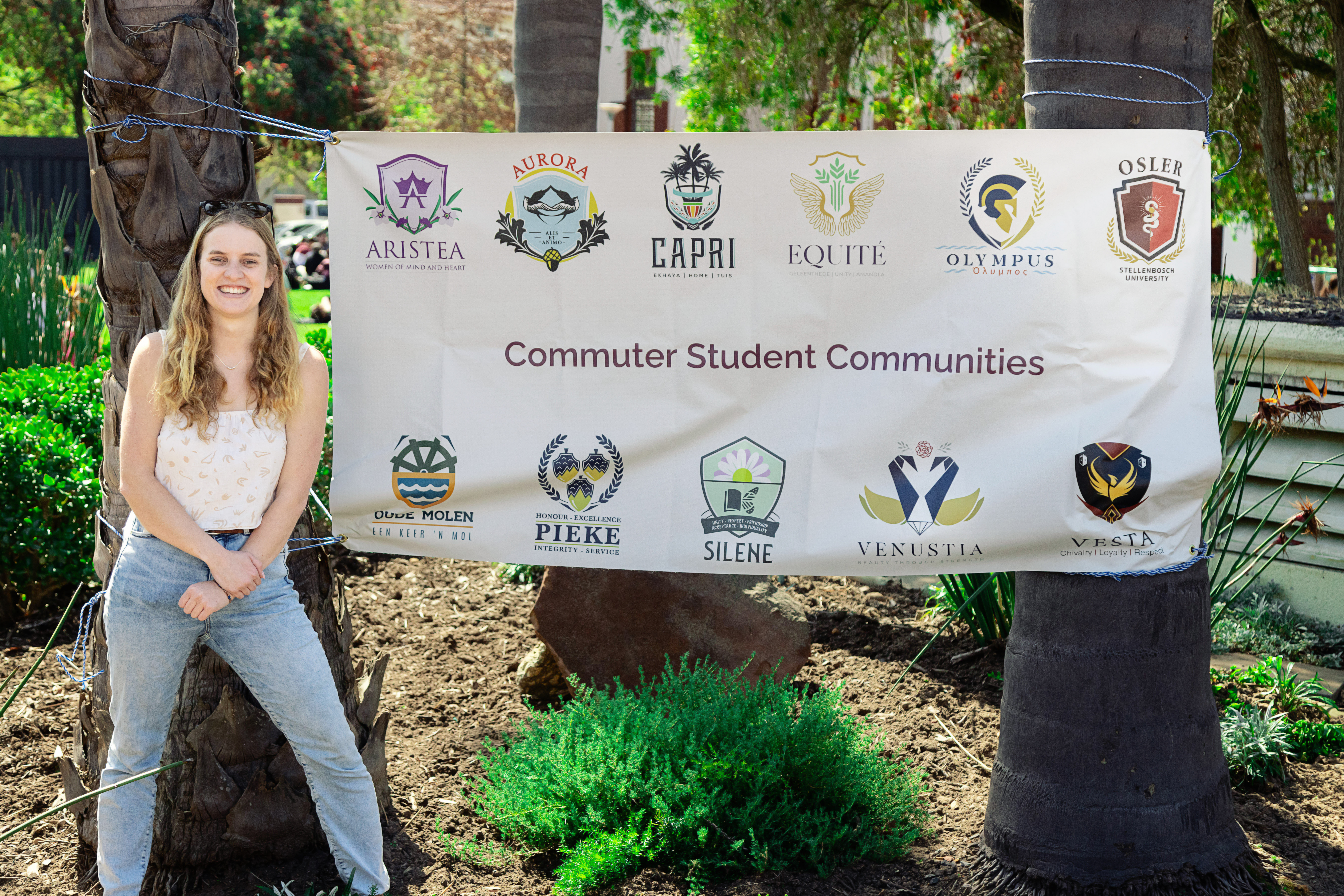Photo of student standing next to banner with commuter student communit names
