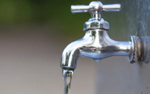 Water tap with water drop outdoor green park background.