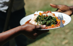 A picture of one person handing a plate of African food to another person.