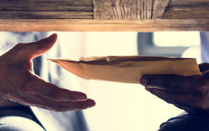 A picture of one hand passing an envelope to another hand under a table.