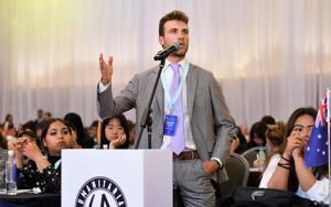 Photo of a male student speaking at a podium at the Humanitarian Affairs Asia University Scholars Leadership Symposium.