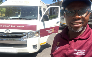 A Photograph of SU International Student and SUI Driver, Moses Shmabare, standing alongside the SU vehicle that he uses to drive international students, partners and staff around Stellenbosch