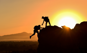 person at the top of a mountain helping someone else up
