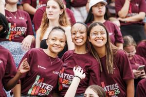 Three newcomers in their 2025 newcomer t-shirts smiling at the camera from the stadium at the Rector's Welcoming event at Coetzenburg.
