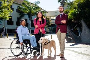 This is a photo of students and staff with disabilities on the Rooiplein. One student is seated in a wheelchair, another has her guide dog with her, and the third student has an invisible disability.