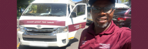 A Photograph of SU International Student and SUI Driver, Moses Shmabare, standing alongside the SU vehicle that he uses to drive international students, partners and staff around Stellenbosch