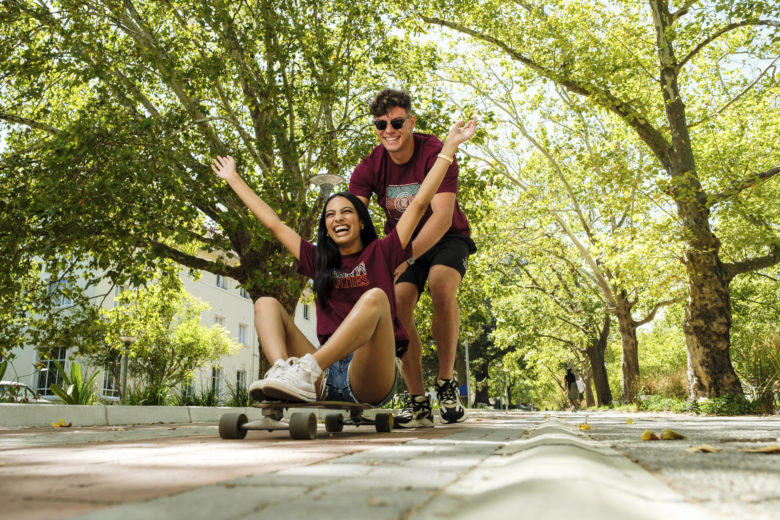 SU Students on victoria street male student pushing female student on a skateboard.
